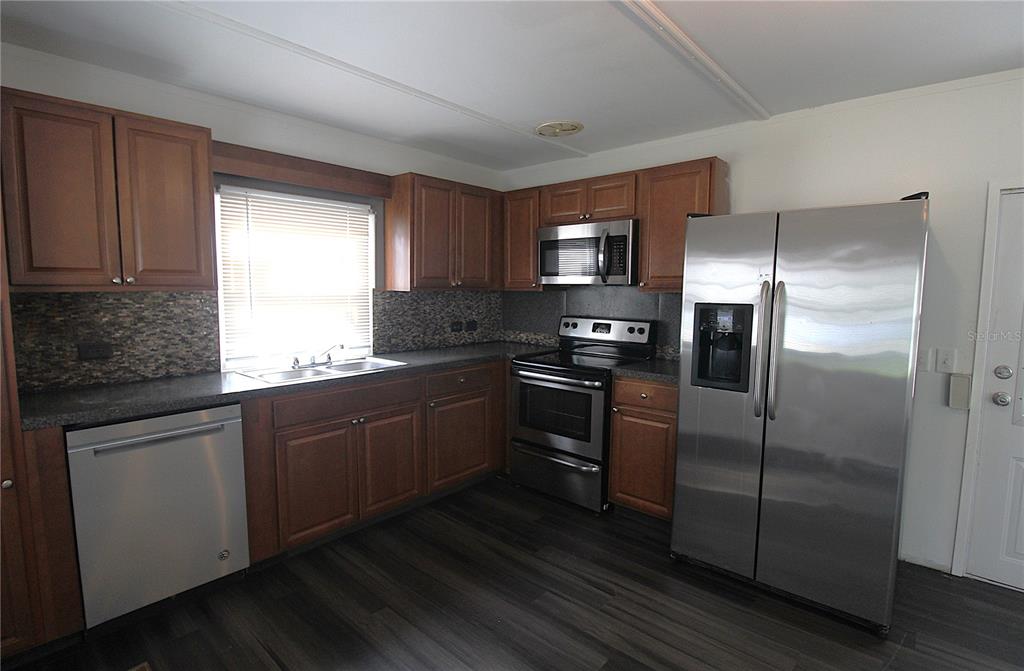 A kitchen features wood cabinets, stainless steel appliances, a dark backsplash, and dark wood flooring — 503 51ST AVENUE W UNIT 503, BRADENTON, FL