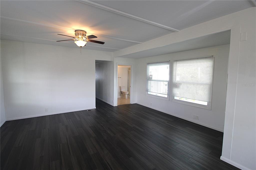 An empty room features dark wood-look flooring, white walls, a ceiling fan, and two windows — 503 51ST AVENUE W UNIT 503, BRADENTON, FL