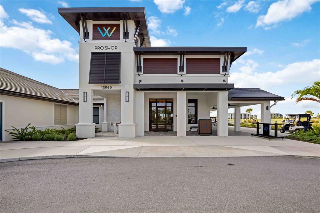 The exterior of a modern clubhouse building features a pro shop entrance and golf cart — 17475 OPAL SAND DRIVE UNIT 207, VENICE, FL