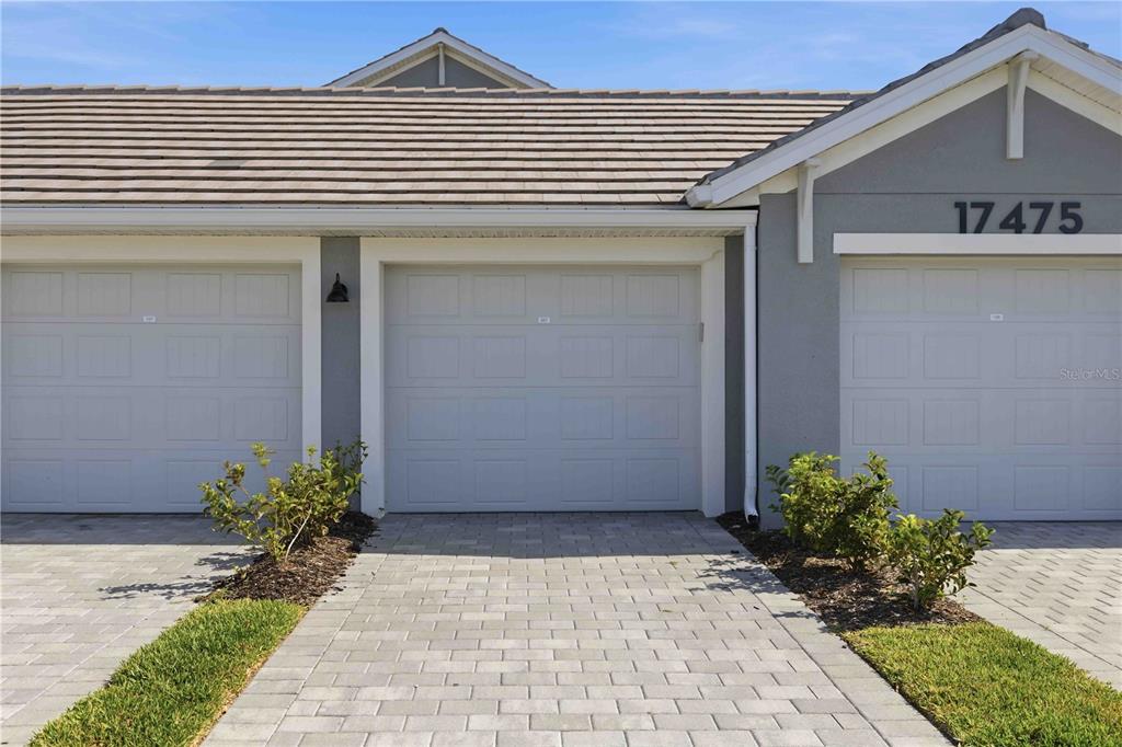A view of three garage doors with a paver driveway and small shrubs in front — 17475 OPAL SAND DRIVE UNIT 207, VENICE, FL