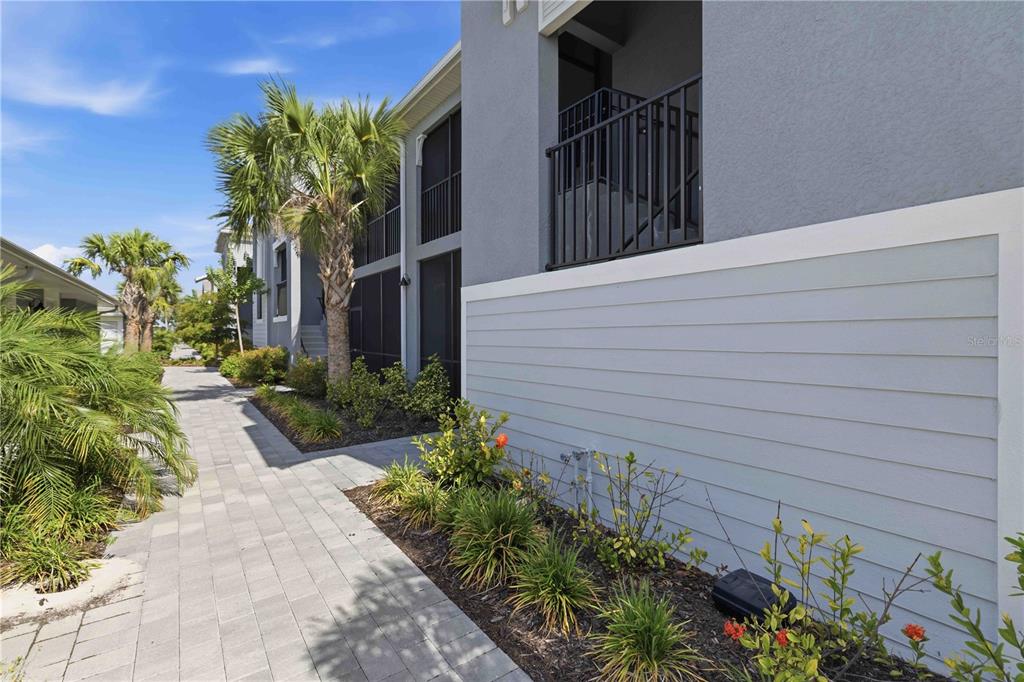 A paved walkway leads past a multi-story building with gray siding and a black railing — 17475 OPAL SAND DRIVE UNIT 207, VENICE, FL
