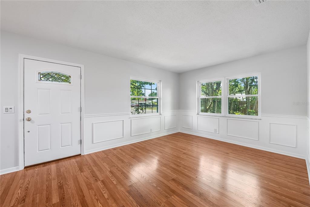An empty room features light gray walls with white wainscoting and polished wood flooring — 7402 WISHING WELL COURT, TAMPA, FL