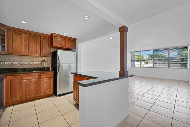 A kitchen with wood cabinets and a breakfast bar opens to a tiled living area — 2175 NE 170th St # 206, North Miami Beach FL 33162, NORTH MIAMI BEACH, FL