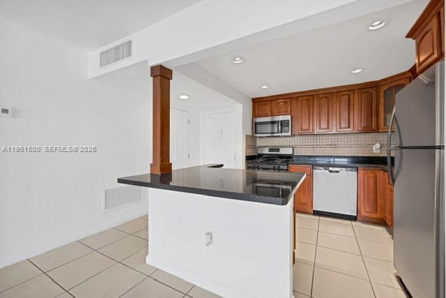 A kitchen features wood cabinets, stainless steel appliances, a black countertop, and tile flooring — 2175 NE 170th St # 206, North Miami Beach FL 33162, NORTH MIAMI BEACH, FL