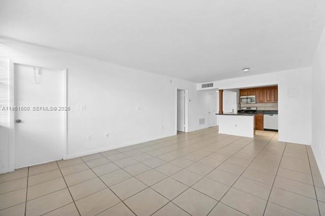 An open-concept living area with light-colored tile flooring leads to a kitchen with wooden cabinets — 2175 NE 170th St # 206, North Miami Beach FL 33162, NORTH MIAMI BEACH, FL