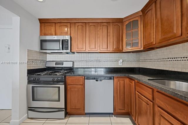 A kitchen features wooden cabinets, stainless steel appliances, dark countertops, and a tiled backsplash — 2175 NE 170th St # 206, North Miami Beach FL 33162, NORTH MIAMI BEACH, FL