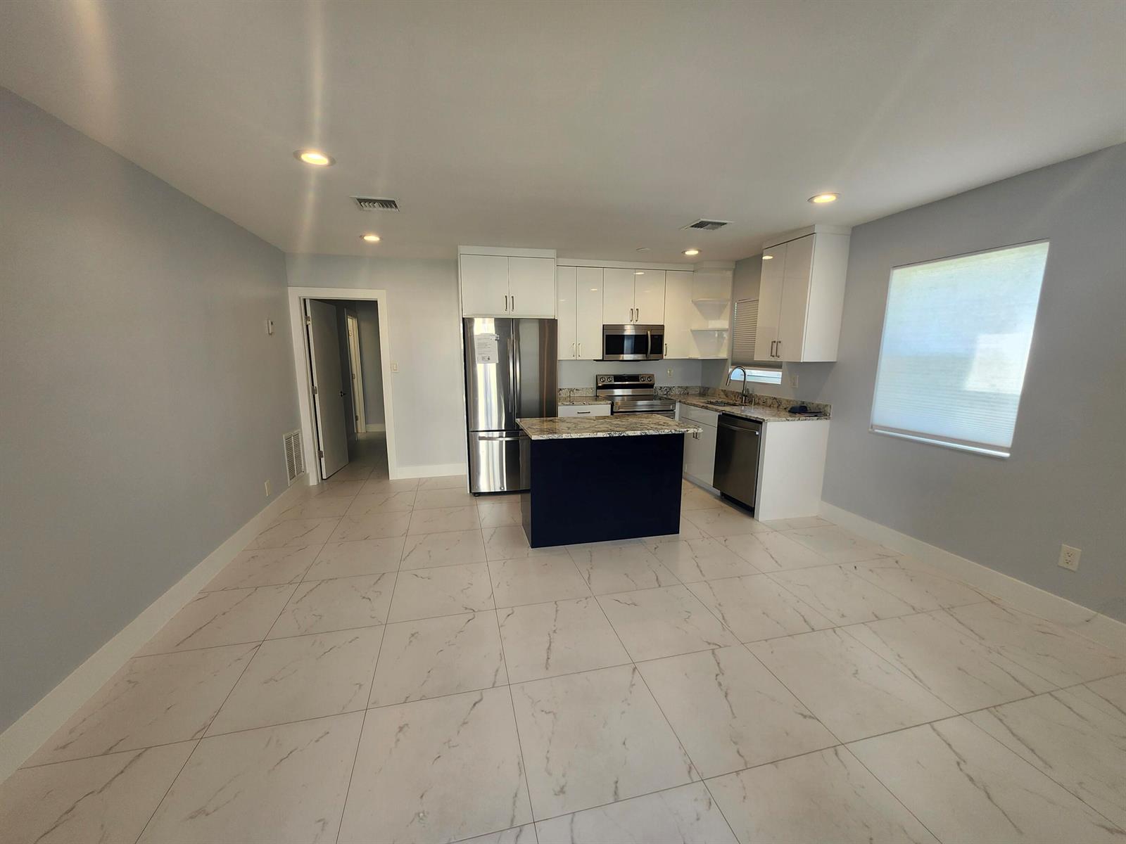 A kitchen features white cabinets, stainless steel appliances, a dark island, and light tiled floors — 511 N 60th Way, Hollywood FL 33024, HOLLYWOOD, FL
