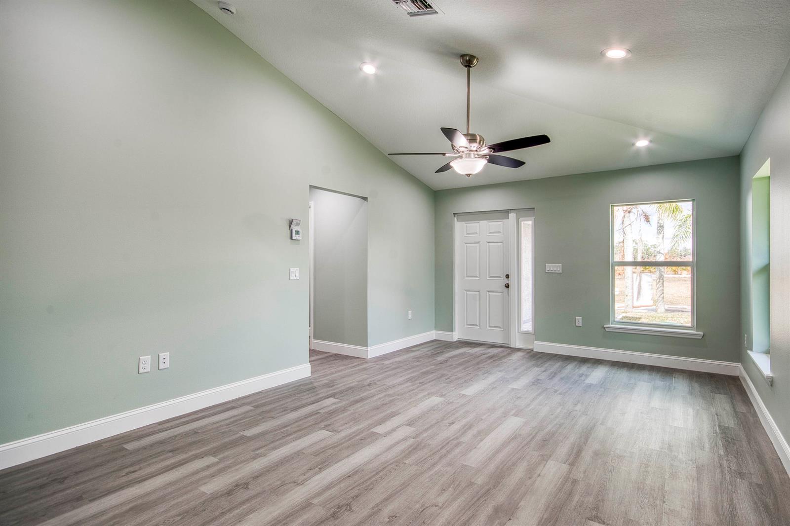 An empty room with vaulted ceilings, light green walls, and gray wood-look flooring — 5108 SE 42nd Street, Okeechobee FL 34974, OKEECHOBEE, FL