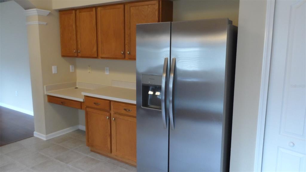 A stainless steel refrigerator stands next to wooden cabinets and a counter in a kitchen — 30709 LANESBOROUGH CIRCLE, WESLEY CHAPEL, FL