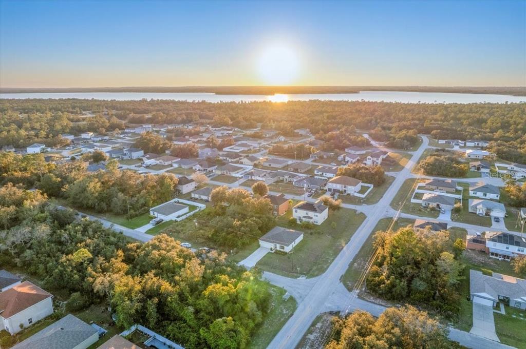 An aerial view shows a residential neighborhood with houses, trees, and a lake at sunset — 1200 WAHNETA DRIVE, KISSIMMEE, FL