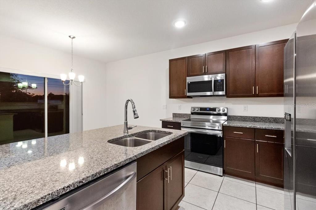 A kitchen with dark wood cabinets, granite countertops, an island, and white tile flooring — 1200 WAHNETA DRIVE, KISSIMMEE, FL
