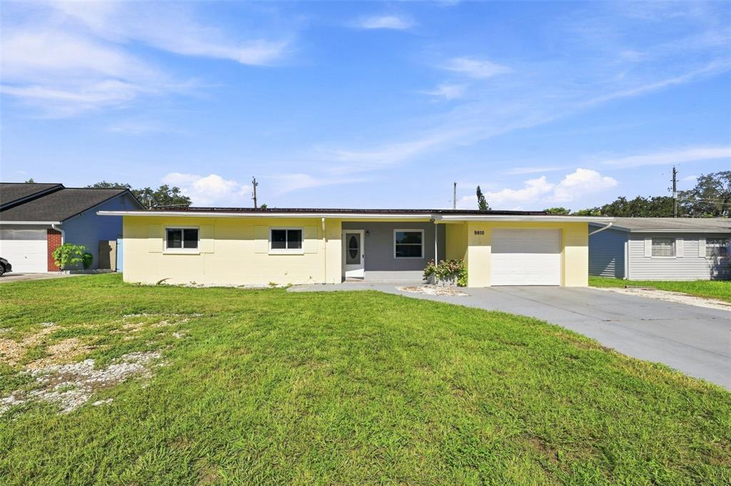 A single-story yellow house with a gray entryway and an attached garage sits on grass — 9810 N 54TH STREET, TEMPLE TERRACE, FL