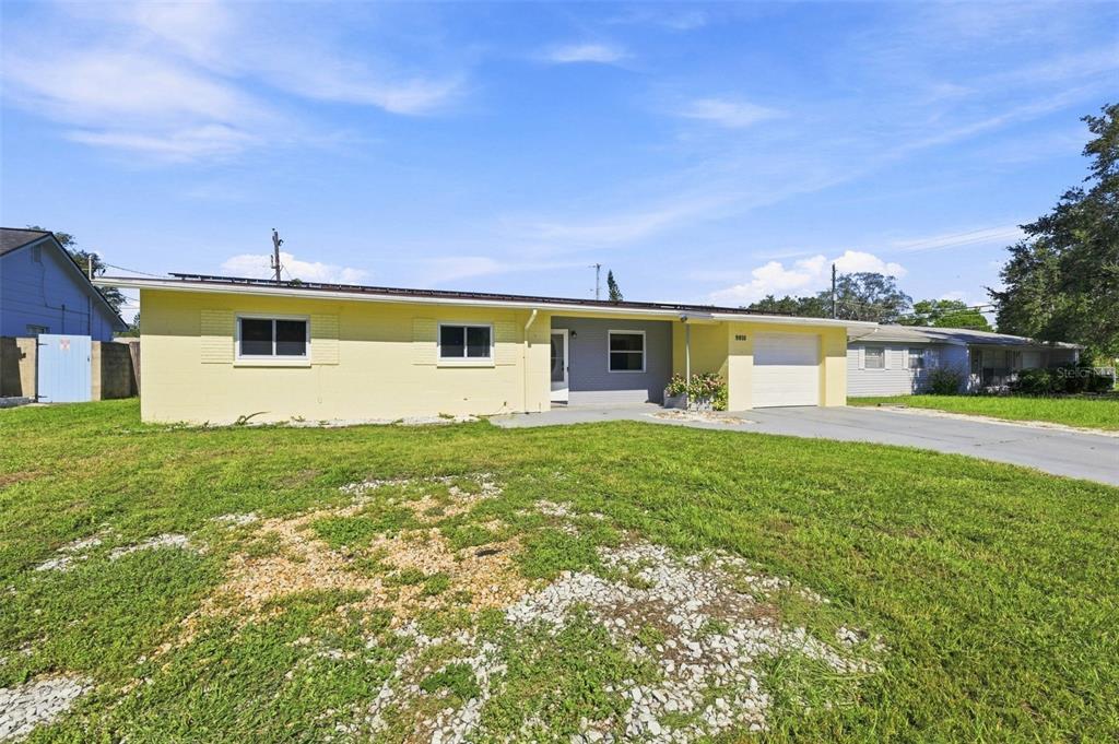 A single-story yellow house with a gray front section, a garage, and a front lawn — 9810 N 54TH STREET, TEMPLE TERRACE, FL