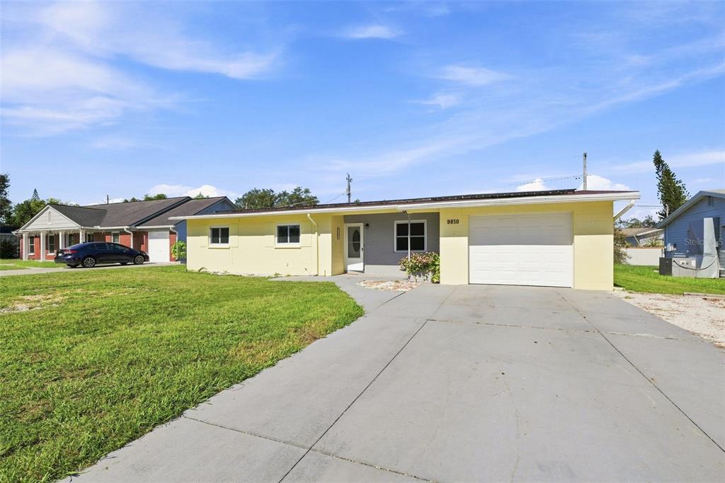 A single-story house with yellow siding, a white garage door, and a concrete driveway — 9810 N 54TH STREET, TEMPLE TERRACE, FL