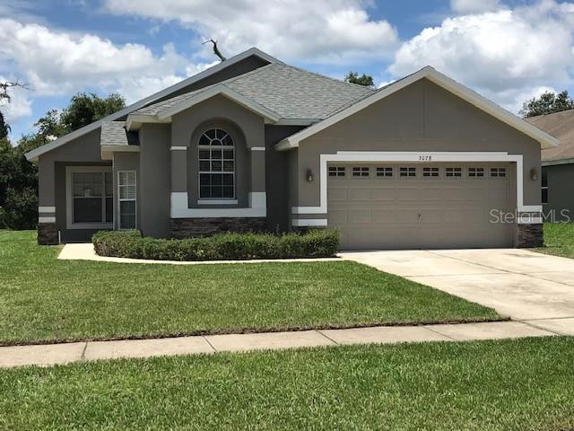 A single-story house with a tan stucco exterior, a two-car garage, and a front lawn — 3078 VERBENA DRIVE, DELTONA, FL