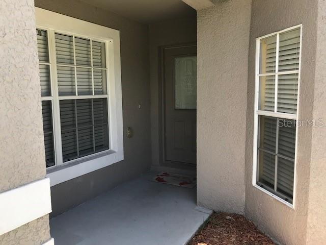 A covered entryway features a front door, two windows with blinds, and concrete flooring — 3078 VERBENA DRIVE, DELTONA, FL