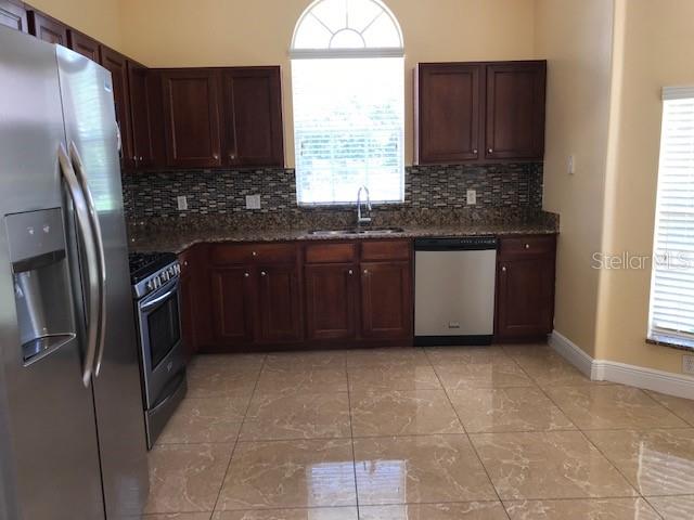 A kitchen features dark wood cabinets, stainless steel appliances, granite countertops, and light-colored tile flooring — 3078 VERBENA DRIVE, DELTONA, FL