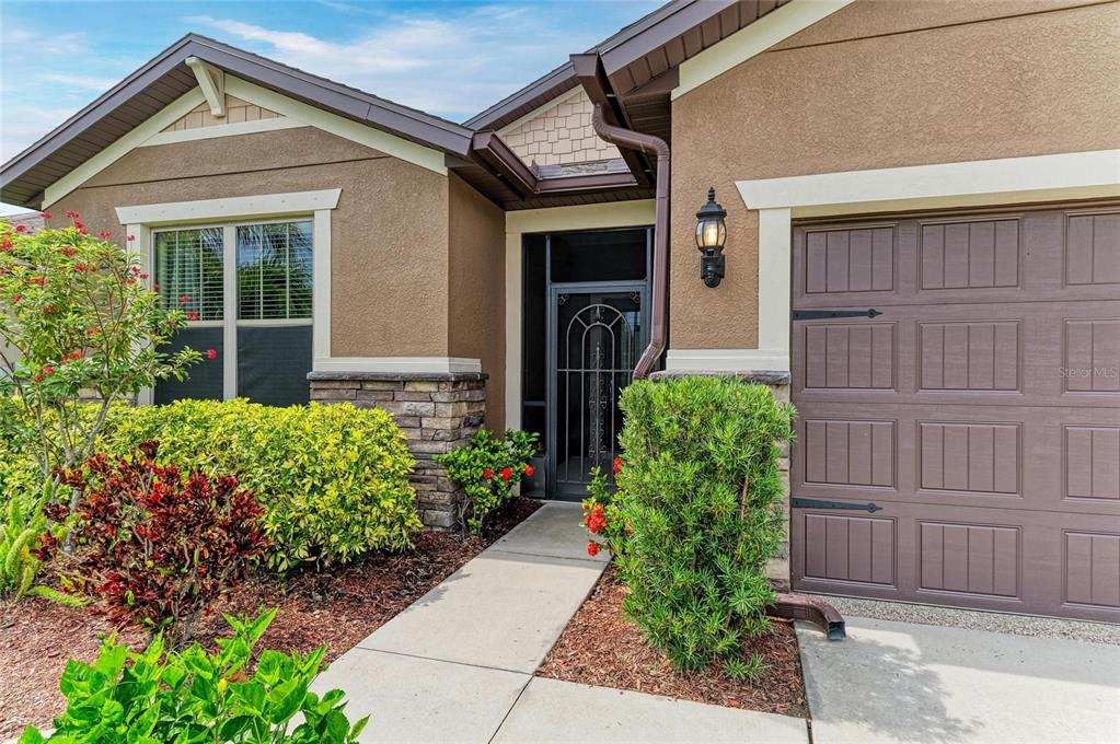 A tan stucco house exterior features a stone base, a brown garage door, and landscaping — 10708 52ND COURT E, PARRISH, FL
