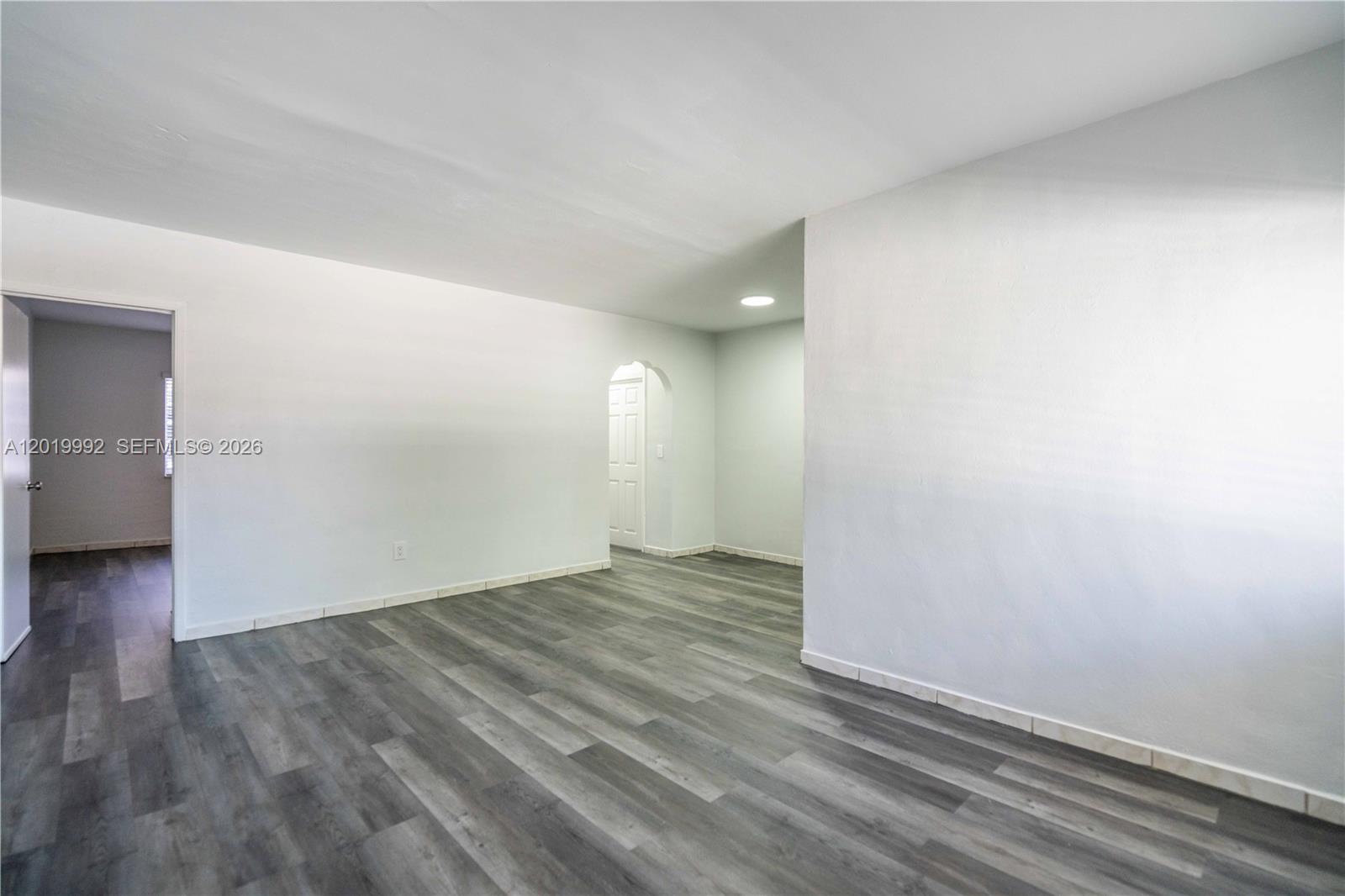 An empty room features white walls, gray wood-look flooring, and an arched doorway — 7911 Abbott Ave # 9, Miami Beach FL 33141, MIAMI BEACH, FL