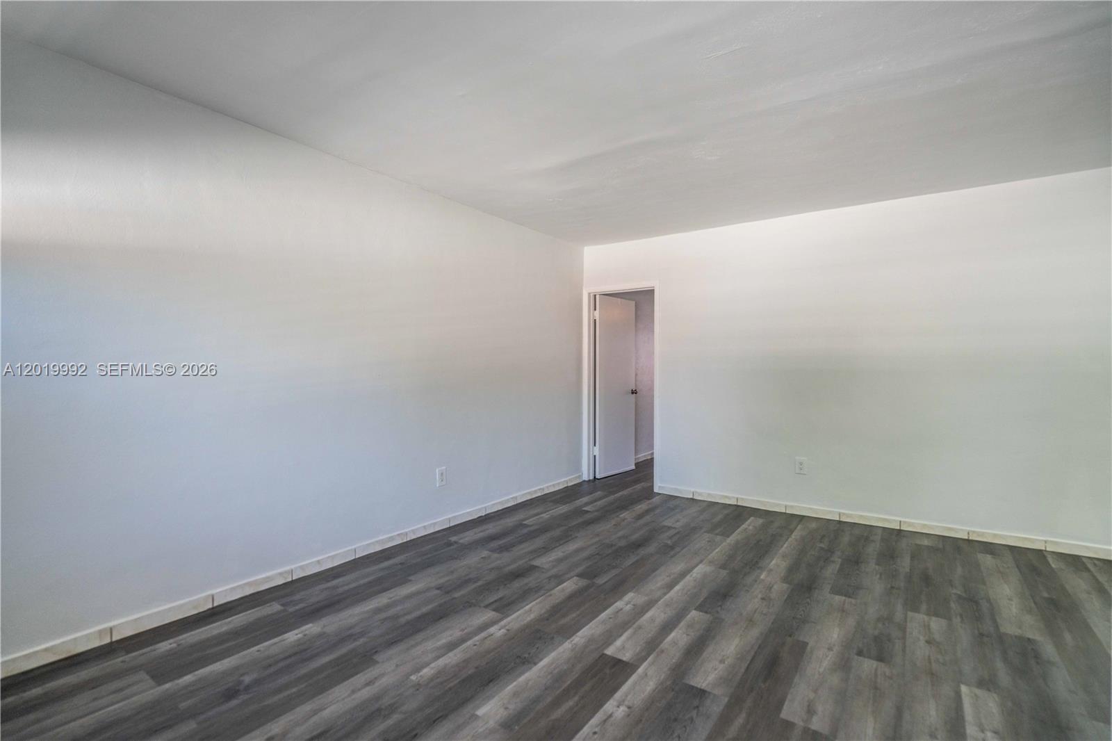 An empty room features white walls, gray wood-look flooring, and a single open doorway — 7911 Abbott Ave # 9, Miami Beach FL 33141, MIAMI BEACH, FL