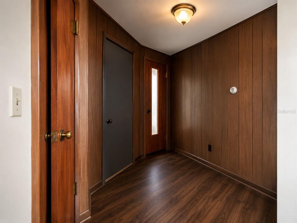 A hallway features wood-paneled walls, dark wood-look flooring, a ceiling light, and three doors — 8428 ANAY COURT, NEW PORT RICHEY, FL