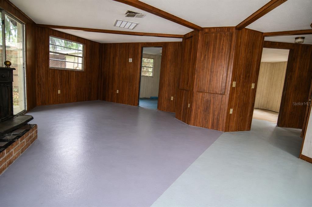 A living room features wood-paneled walls, a brick fireplace base, and painted gray floors — 8428 ANAY COURT, NEW PORT RICHEY, FL