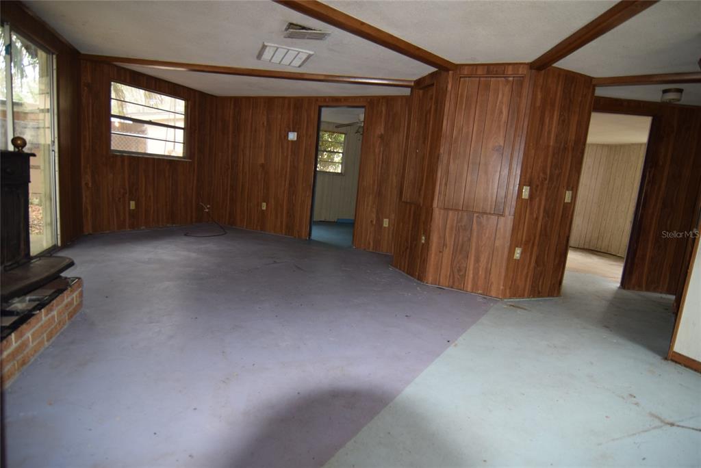 A living room features wood-paneled walls, exposed ceiling beams, and a painted concrete floor — 8428 ANAY COURT, NEW PORT RICHEY, FL