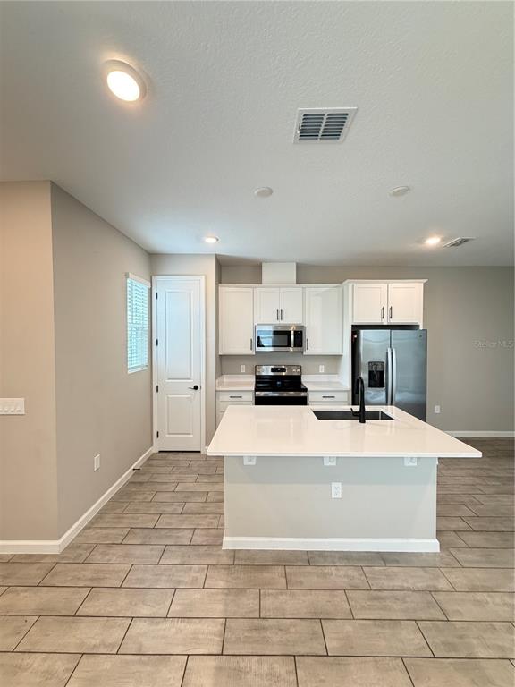 A modern kitchen features white cabinets, stainless steel appliances, and a large central island — 1449 AXEL GRAESON AVENUE, KISSIMMEE, FL