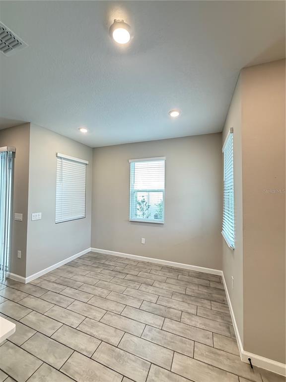 An empty dining area features light gray walls, tile flooring, and three windows with blinds — 1449 AXEL GRAESON AVENUE, KISSIMMEE, FL