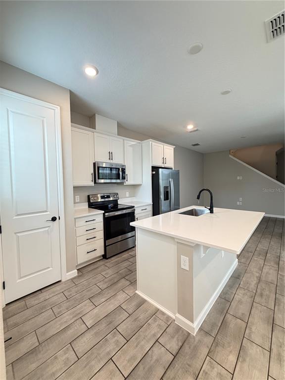 A kitchen features white cabinetry, stainless steel appliances, a center island, and wood-look tile flooring — 1449 AXEL GRAESON AVENUE, KISSIMMEE, FL