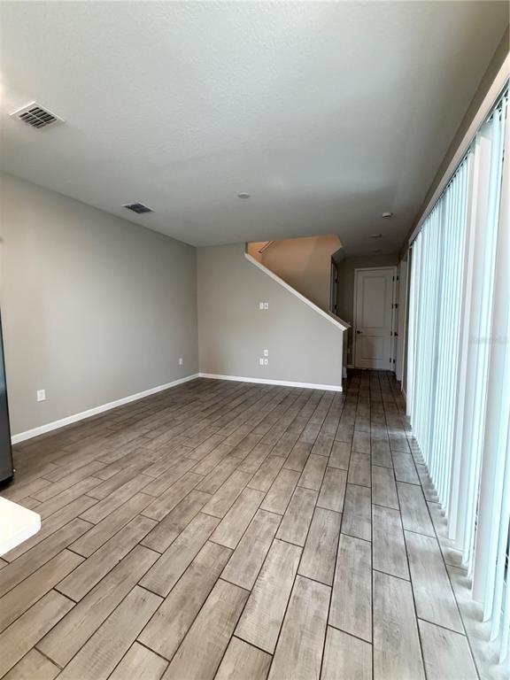 An empty room with light-colored walls, wood-look tile flooring, and a staircase leading upstairs — 1449 AXEL GRAESON AVENUE, KISSIMMEE, FL