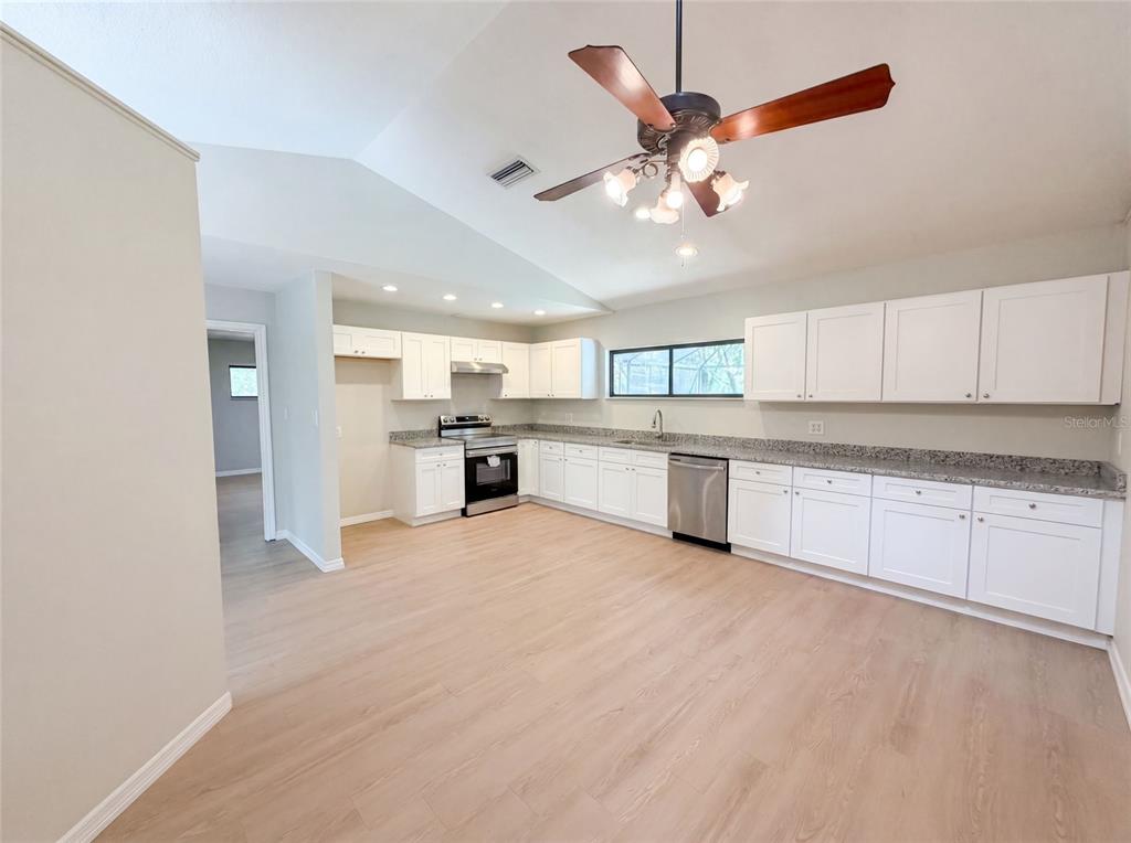 A kitchen with white cabinets, granite countertops, stainless steel appliances, and light wood-look flooring — 3739 LAKE GRIFFIN ROAD, LADY LAKE, FL