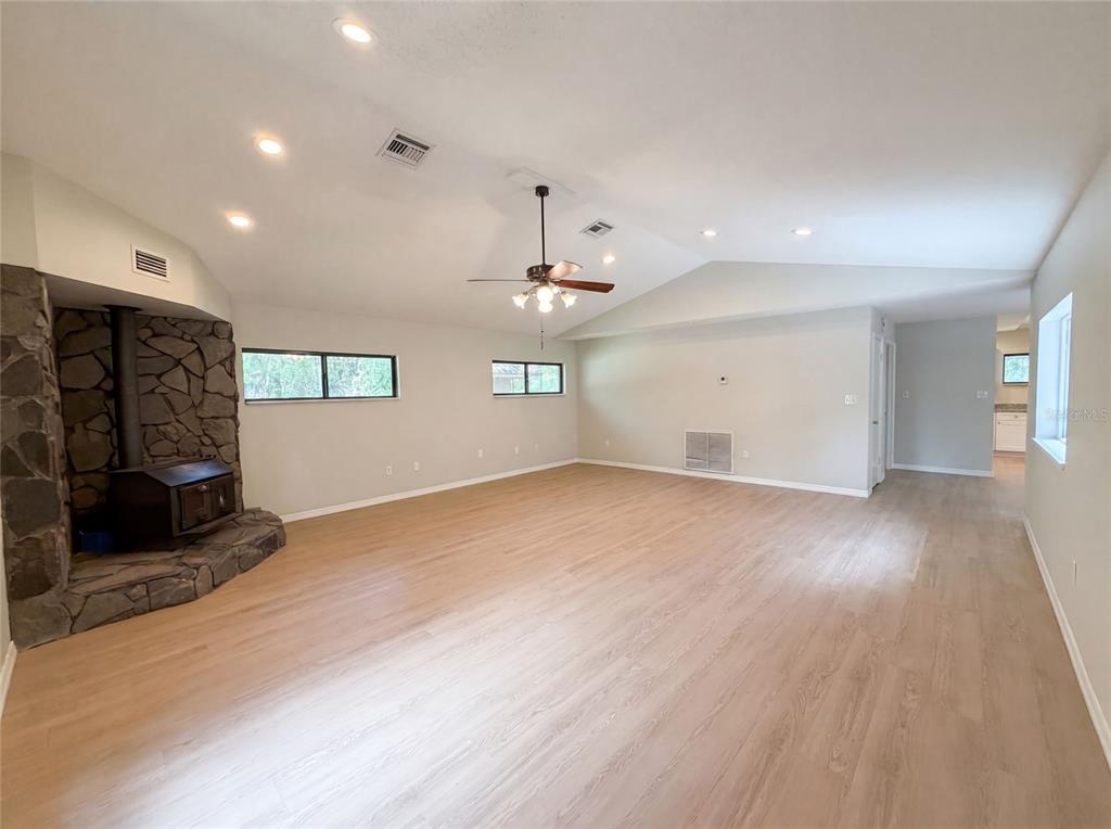 A spacious living room features light wood-look flooring, a stone fireplace, and a vaulted ceiling — 3739 LAKE GRIFFIN ROAD, LADY LAKE, FL