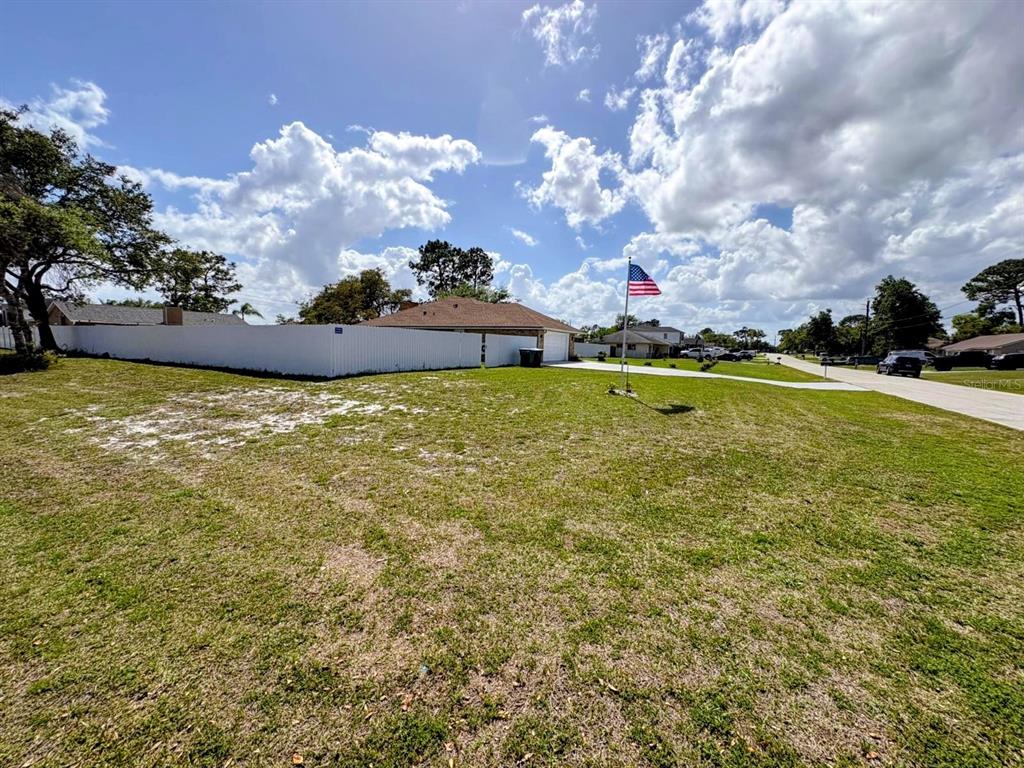 A grassy residential lot features a white fence, an American flag, and a nearby house — 3958 CARRICK BEND DRIVE,, KISSIMMEE,, FL