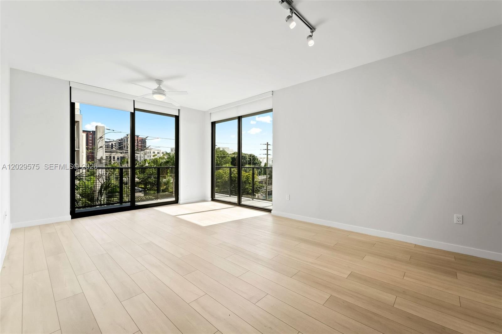 An empty room features light wood-look flooring, white walls, a ceiling fan, and sliding glass doors — FORT LAUDERDALE, FL
