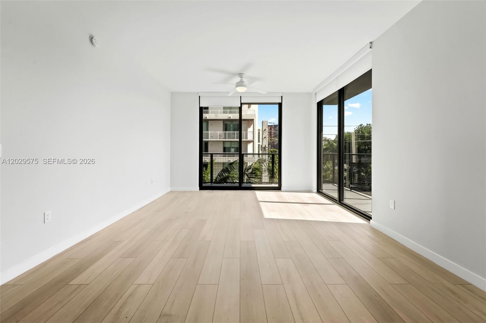 An empty room features light wood-look flooring, white walls, a ceiling fan, and sliding glass doors — FORT LAUDERDALE, FL