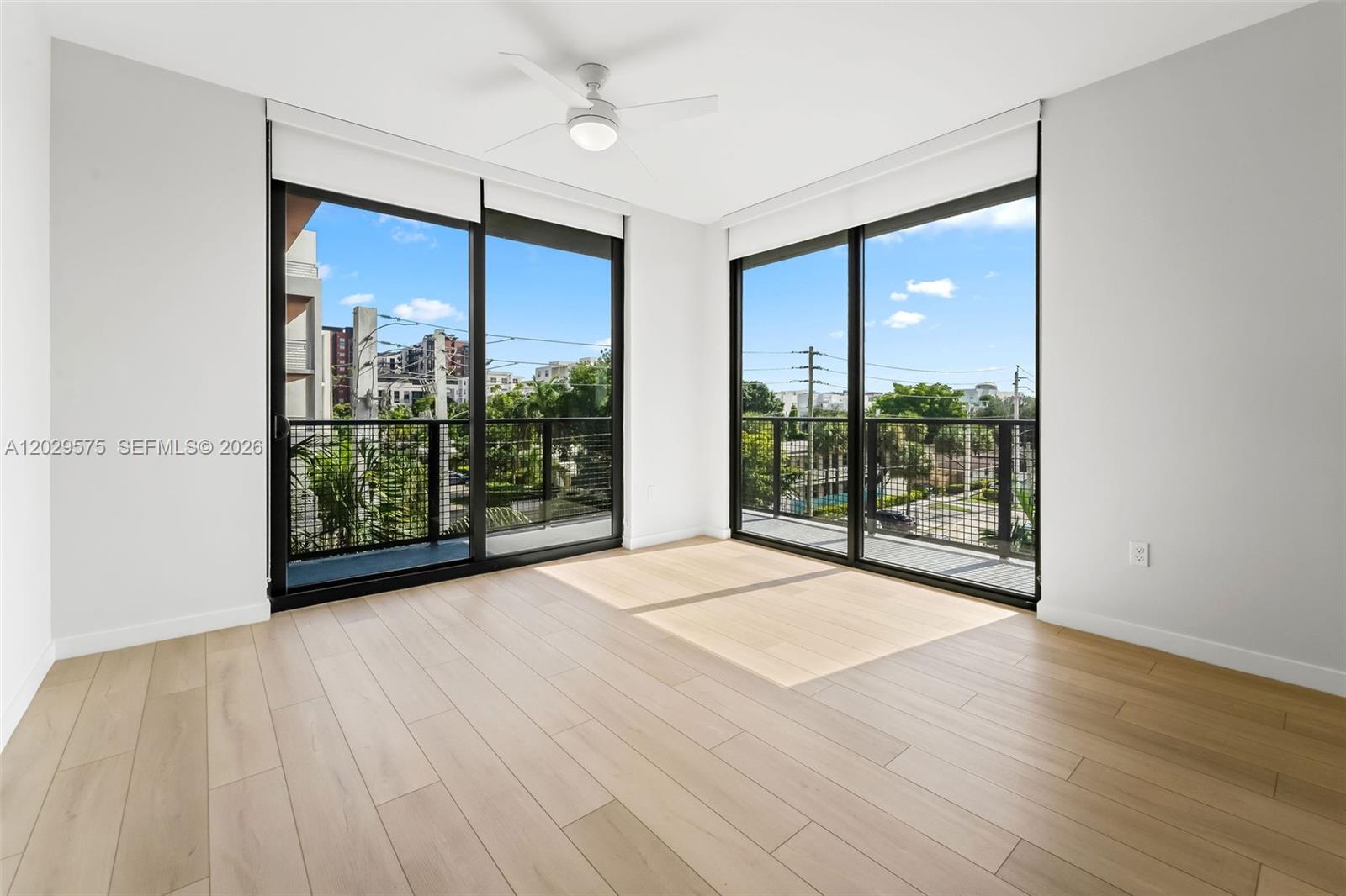 An empty room features light wood flooring, a ceiling fan, and large sliding glass doors — FORT LAUDERDALE, FL