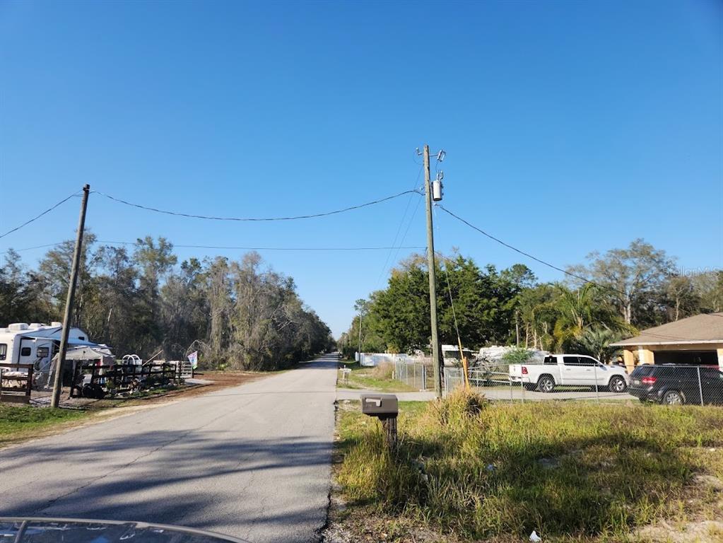 A paved road stretches between a residential property with a parked truck and wooded areas — LOT 19 NW 119 TH COURT, OCALA, FL