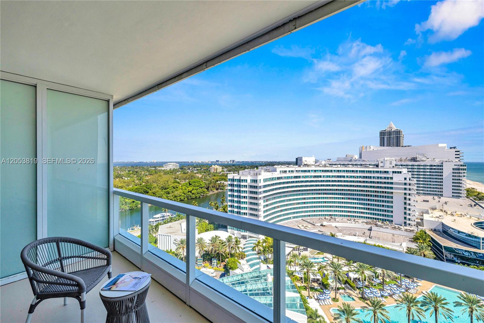 A balcony with a gray chair and table overlooks a large curved hotel and pool — 4391 COLLINS AVE # 1706, Miami Beach FL 33140, MIAMI BEACH, FL