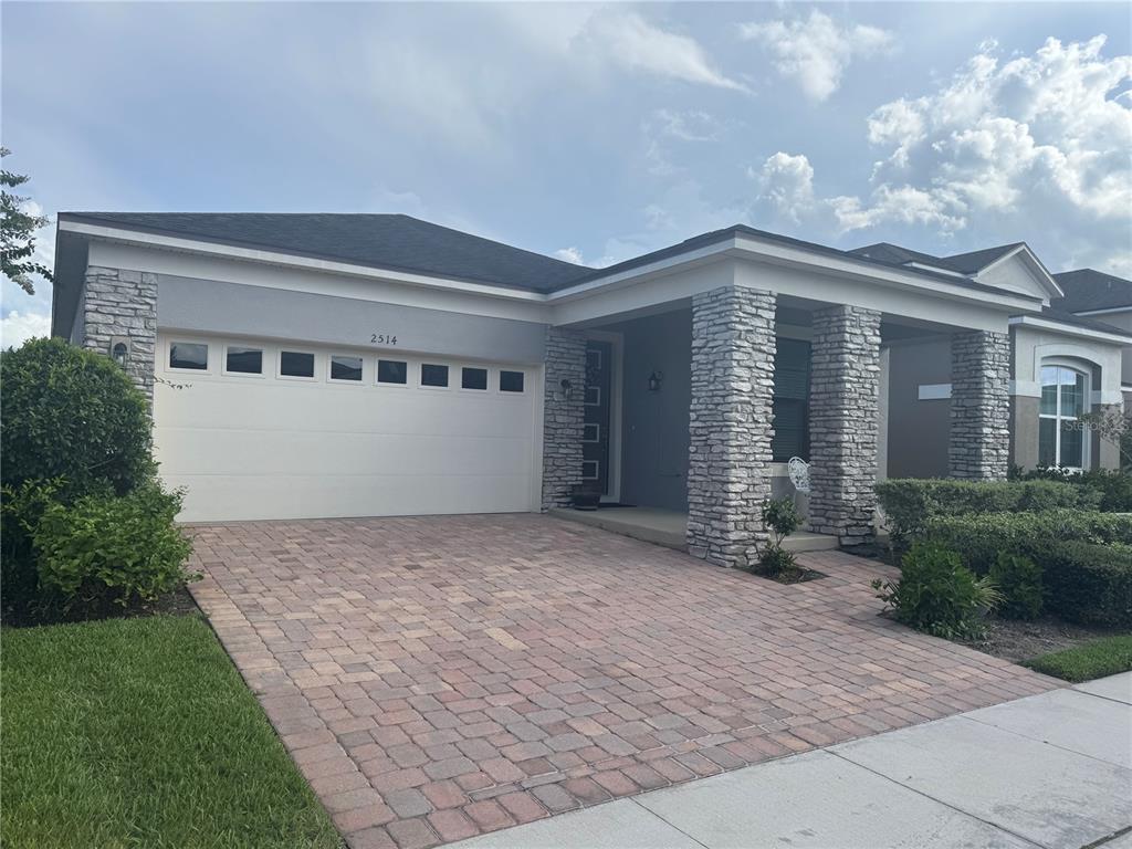 A single-story house features a stone-accented facade, a two-car garage, and a paved driveway — 2514 NOUVEAU WAY, KISSIMMEE, FL
