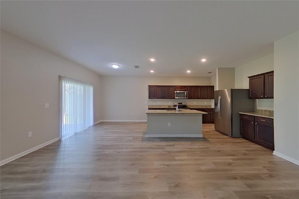 An open-concept kitchen and living area features dark wood cabinets, granite countertops, and light flooring — 15724 PINE SISKIN LOOP, MASCOTTE, FL