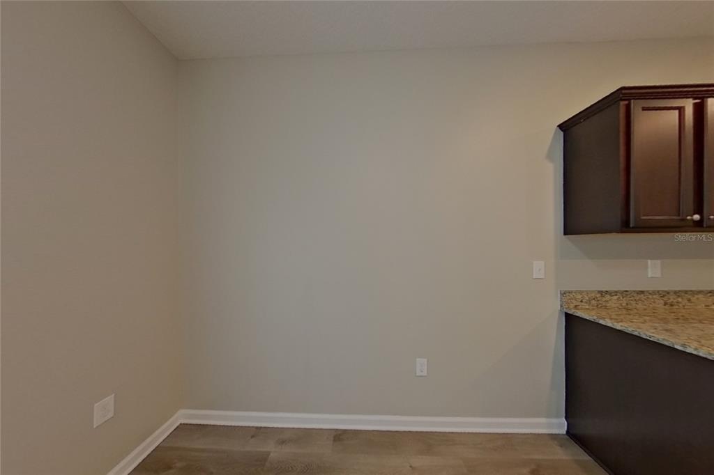 An empty room with light walls, wood-look flooring, and dark kitchen cabinets with granite countertops — 15724 PINE SISKIN LOOP, MASCOTTE, FL