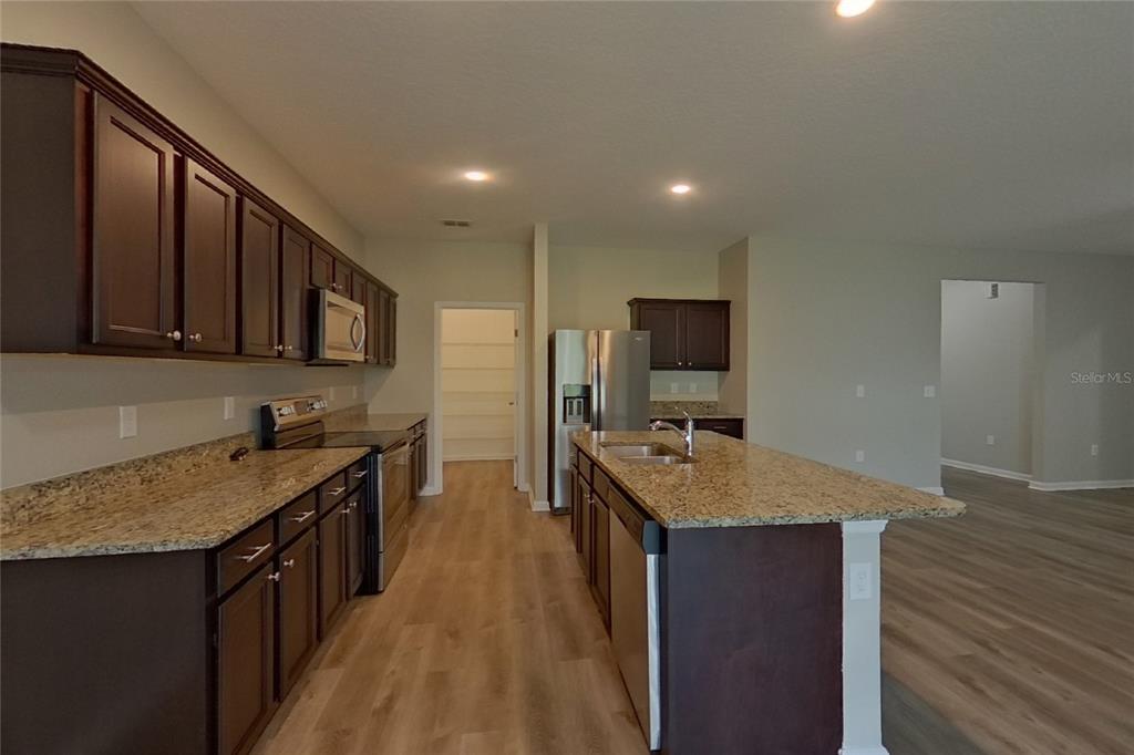 A kitchen features dark wood cabinets, granite countertops, a center island, and stainless steel appliances — 15724 PINE SISKIN LOOP, MASCOTTE, FL