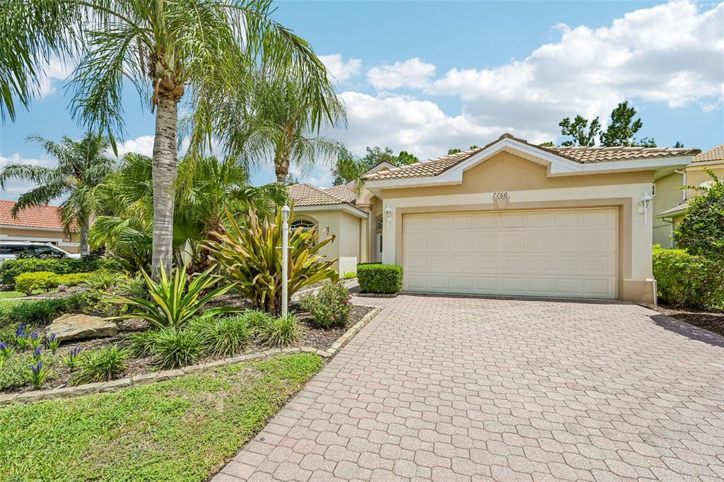 A single-story house with a beige stucco exterior, a tiled roof, and a paved driveway — 7760 US OPEN LOOP, LAKEWOOD RANCH, FL