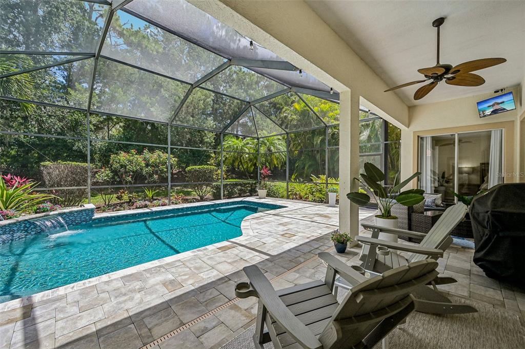 A covered patio features a swimming pool with a water feature inside a screened enclosure — 7760 US OPEN LOOP, LAKEWOOD RANCH, FL