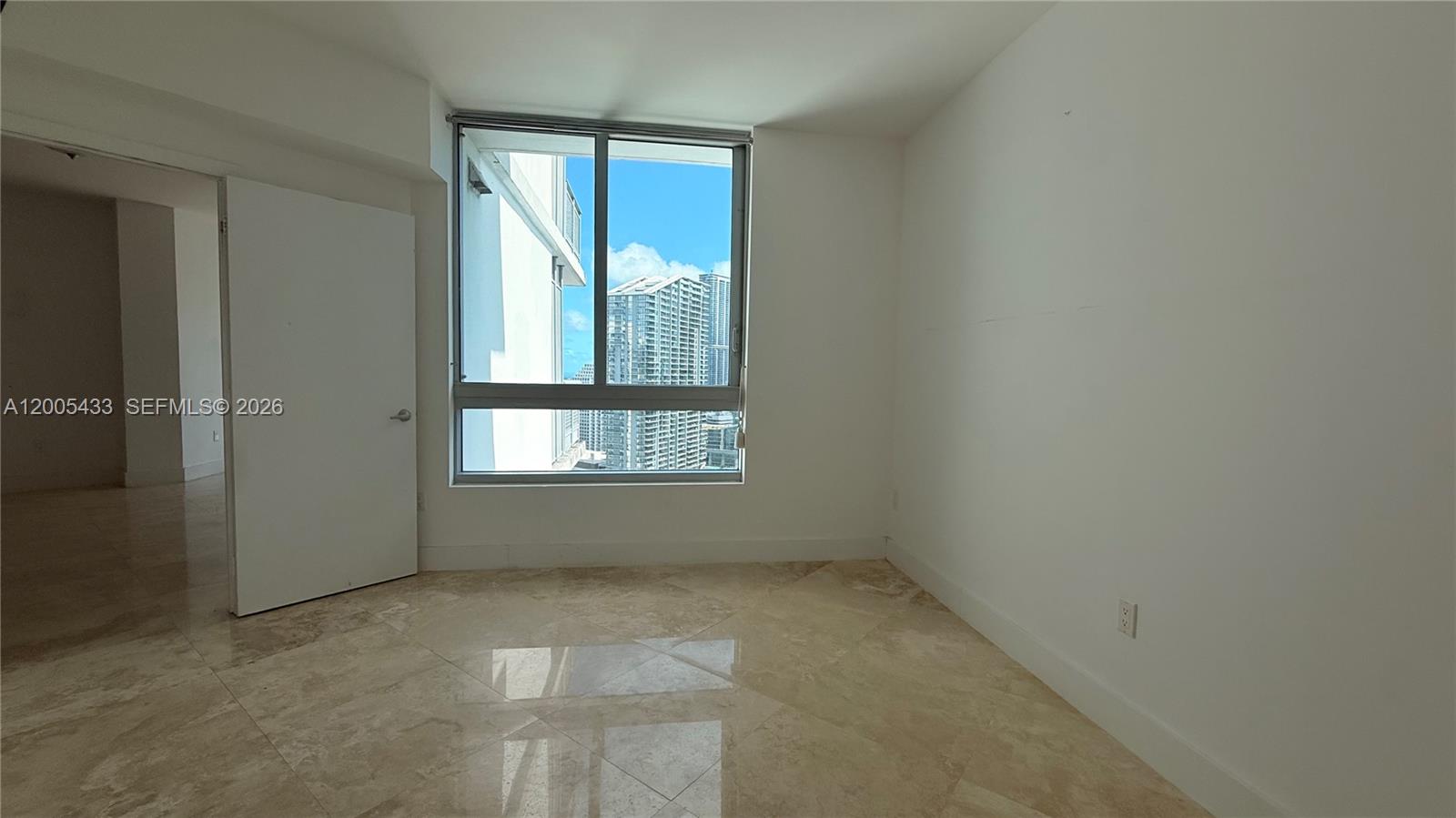 An empty room features light-colored tile flooring, white walls, and a window overlooking city buildings — 350 S Miami Ave # 3608, Miami FL 33130, MIAMI, FL