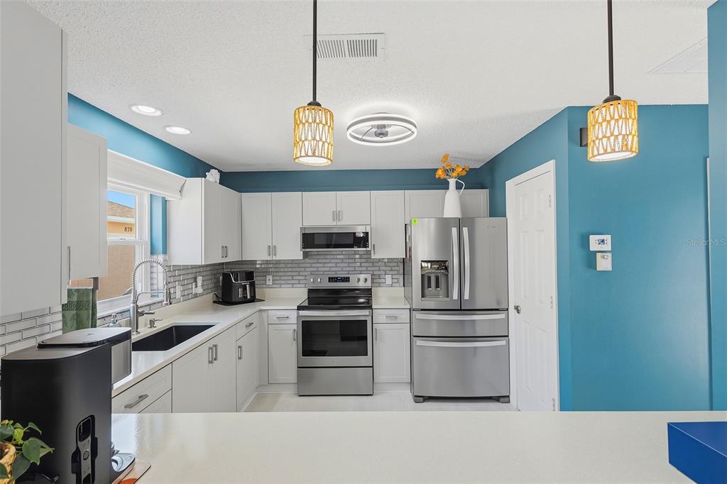 A kitchen features white cabinets, stainless steel appliances, a subway tile backsplash, and blue walls — 868 OVIEDO ROAD, THE VILLAGES, FL