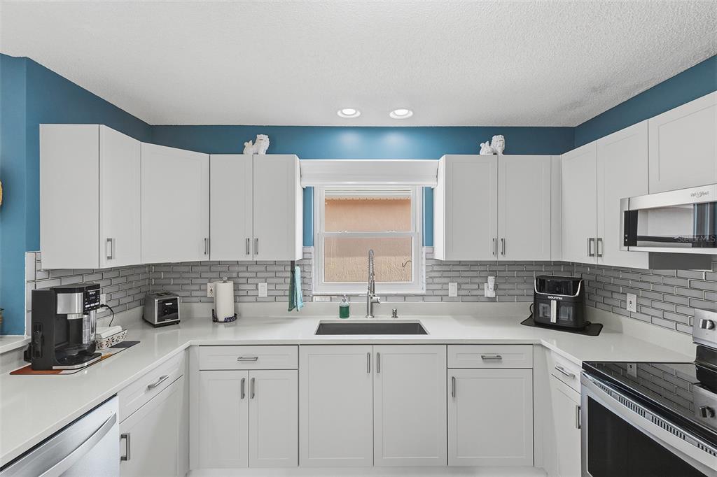 A kitchen features white cabinets, gray subway tile backsplash, quartz countertops, and stainless steel appliances — 868 OVIEDO ROAD, THE VILLAGES, FL