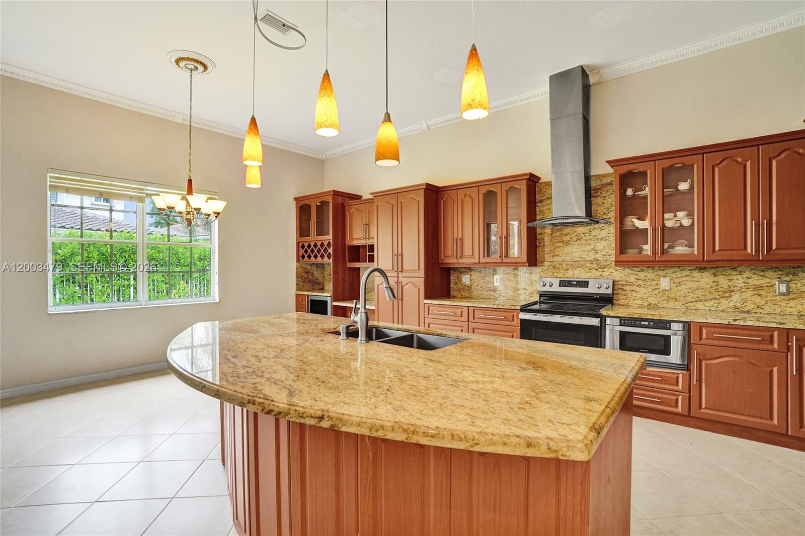 A kitchen features wood cabinets, granite countertops, a large island, and four pendant lights — 1169 Peregrine Way, Weston FL 33327, WESTON, FL