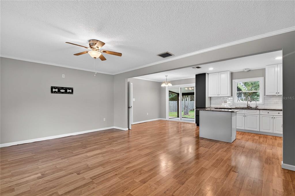 An open-concept living room and kitchen with wood-look flooring, white cabinets, and a ceiling fan — 27638 LISA DRIVE, TAVARES, FL
